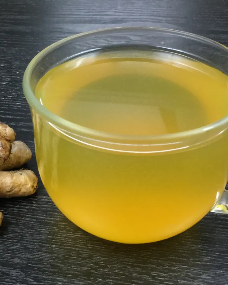چای زنجبیل طلایی کنار ریشه زنجبیل تازه روی میز تیره